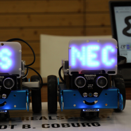 Zwei kleine ferngesteuerte Fahrzeuge mit nach vorne gerichteten Kameras und jeweils einer Platine, auf denen zusammen der Schriftzug RS NEC (staatliche Realschule Neustadt b. Coburg) zu erkennen ist.