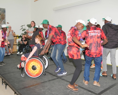 Mehrere Sportler der Special Olympic World Games tanzen mit drei Rollstuhlfahrern auf einer kleinen Bühne.